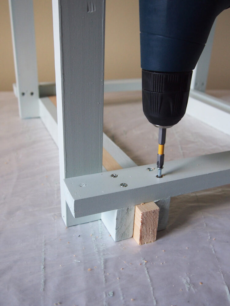 13     Turn the frame over, and using one length of wood as a measuring spacer, secure a piece of wood parallel to the edge of the frame. Drill and screw each end.